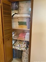 Full view of linen closet filled with various linens, towels, bedspreads, and comforters folded neatly on several shelves to confirm content and color variety.