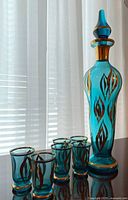 Full set of aqua glass decanter and six aperitif glasses on reflective surface showing gold decoration and overall appearance.
