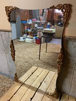 Full view of the large wall mirror with ornate gold-tone sculpted corner decorations, showing the reflective surface and size relative to surroundings.