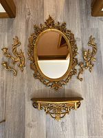 Full set displayed on floor showing mirror, two sconces, and shelf with metallic gold finish and ornate details