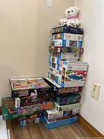 Photo showing stacked boxed jigsaw puzzles with a white stuffed bear on top; multiple varied box designs visible, confirming variety and quantity