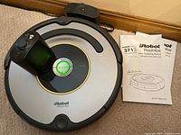 Top-down view of Roomba 600 Series robot vacuum with manuals beside it showing the title and images on pages.