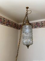 Full view of the swag lamp hanging against corner wall and floral wallpaper, showing chain and ceiling mount.