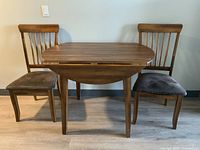 Front view of table with drop leaves down and two wooden chairs with dark cushioned seats.