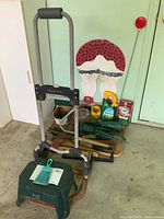 Photo showing green folding utility cart, small plastic stool, garden and household tools alongside garden care products on a wooden cart.