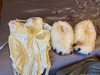 Lot contents including two off white satin and lace bustiers and fuzzy bear feet slippers on bed