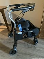 Side view of nearly new walker with tags attached, showing padded seat, handlebars, small caster wheels, and foldable frame.