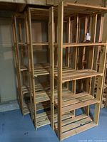 Three natural wood shelving units with multiple slatted shelves in basement setting.