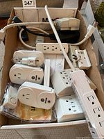 Wide shot showing three Woods wireless remote outlet plugs, a 4-outlet power strip, and other miscellaneous power strips inside a box.