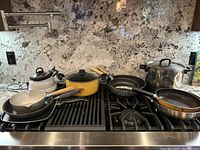 Photo of 10-piece vintage pot and pan set on stove, including enamel and stainless steel pieces with various handles and lids