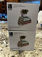 Two unopened boxes of Umbra Conceal Large Invisible Book Shelf sets stacked on a countertop, showing product labeling and design image.