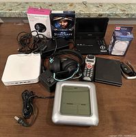 Photo showing full assortment of electronics including DVD player, headphones, game, routers, charger, and cables on a table
