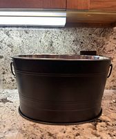 Front view of black insulated beverage tub ice bucket on countertop.