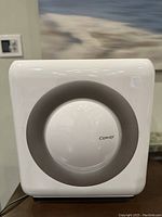 Front view of white Coway air purifier featuring a gray circular element and Coway logo in the center.