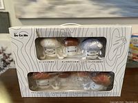Front view of the box showing the six Dokomodake plush figures inside a windowed package with wood grain design background and Japanese text.