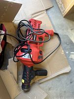 Red and black hand-held electric drain cleaner with attached cable, placed on cardboard.