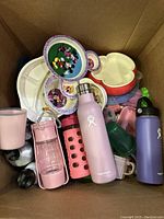 Box containing multiple assorted water bottles and Disney-themed plastic bowls including pink and purple Hydro Flask bottles and Mickey Mouse divided plates.