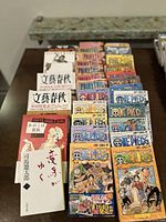 Top-down photo showing a stack of Japanese manga volumes including One Piece and other titles, with multiple volumes in original sleeves.