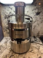 Full front view of the stainless steel Jack La Lannes juicer on a kitchen counter, showing the chute and spout.