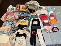 Full lot overview showing various American Girl doll clothes including dresses, tops, leggings, and accessories laid out on a table.