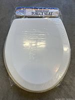 Photo of white molded wood toilet seat wrapped in plastic, with cardboard packaging showing the product name.