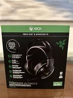 Front view of box showing Razer Thresher Ultimate headset for Xbox One with key features like 7.1 surround sound, 2.4 GHz wireless connection, up to 16 hours battery life, and Pure Digital Audio.