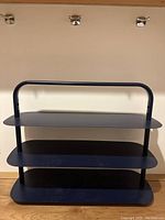 Blue three-tier metal entryway rack positioned against wall under hooks