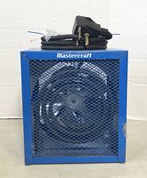 Front view of blue metal Mastercraft garage heater with mesh grille, fan visible inside, and power cord coiled on top.