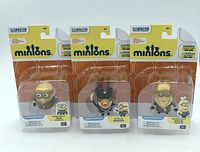 Three Minion action figures in original packaging showing front view with clear plastic covering and cardboard backing.