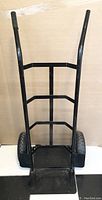 Front view of black heavy duty hand truck showing steel frame, two large pneumatic tires and foldable toe plate