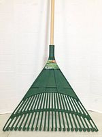 Full view of green plastic rake head with wooden handle against white background.