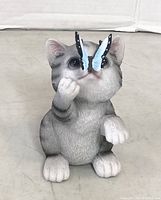 Front view of a gray and white resin cat garden statue with a blue and black butterfly perched on its nose.