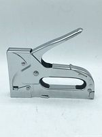 Metal staple tool photographed from side angle showing lever, handle and staple slot.