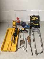 Photo showing various hand tools including tape measure, chalk line, clamps, a hacksaw, measuring squares, screwdriver, and tool tray.