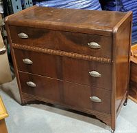 Front and side view of the antique wooden veneer dresser with cup handles on four drawers and caster wheels.