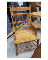 Light brown wooden arm chair with caned seat, decorative carved back, vertical spindles, turned legs and supports
