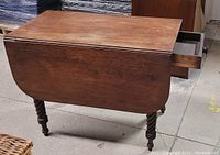 Front side view of the mahogany drop leaf table showing one leaf dropped and the small drawer open.