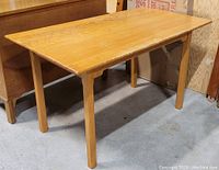 Full view of the rectangular birdseye maple table showing the top surface and legs, placed indoors on a concrete floor.