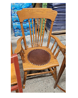 Front view of press back style rocking chair with wooden frame and round leather seat insert with metal studs.