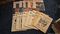 Multiple copies of Galaxy Magazine from 1994 along with vintage Comics The Golden Age and Comic Strip News magazines arranged on blue cloth.