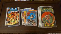 Three stacks of comics including Warlord and Arak Son of Thunder series, with annuals visible, photographed on wooden surface.