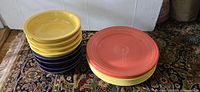 Photo showing stacked yellow plates and bowls with purple bowls, plus redish/orange plates.