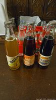 Three unopened vintage Russian soda glass bottles displayed front, showing yellow/orange, orange, and dark-colored sodas with paper labels.