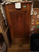 Front view of the antique single panel wooden dresser cabinet with the door closed and a white lace cloth partially covering the top.