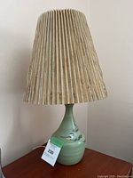 Full view of the ceramic base table lamp with pleated lampshade placed on wooden surface.