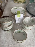 Stack of small bowls and plates with green and white floral pattern and gold accent wrapped in plastic.