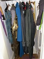 Photo showing multiple jackets and coats hanging in a closet including a blue wool coat, gray shearling suede coat, metallic gold jacket, and other dark-colored outerwear