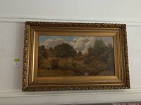 Front view of landscape oil painting in gilt frame hung on wall with lot sticker
