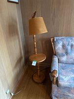 Full view of the Swedish floor lamp with attached round table in pine wood, showing the entire lamp against wood-paneled wall beside a couch.