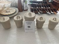 Photo showing five beige vintage stoneware storage jars with screw-on lids arranged in a line on a table.